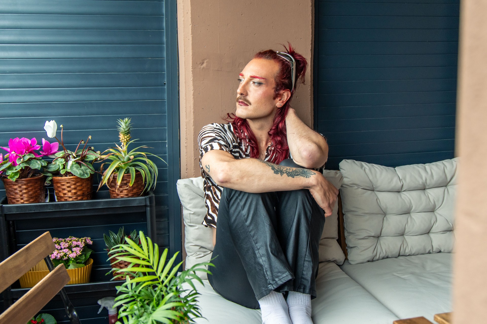 Non-binary person relaxing on a sofa on the balcony and looking away
